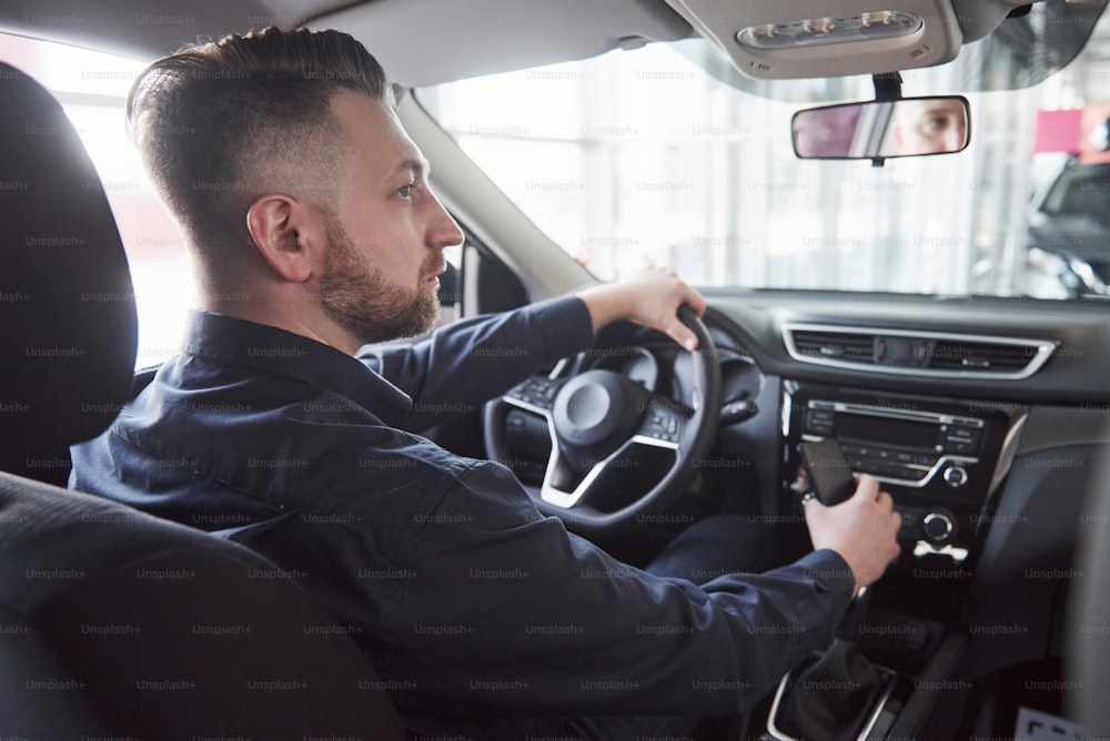 Rear view of young bearded businessman sitting in his luxury black car.