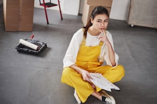 According to a plan I must paint that side of the bulding. Young brunette in the room with white walls and daylight that comes from the window.