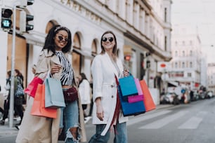 Beautiful stylish girls spending time together and enjoying shopping. They holding colorful paper bags and smiling