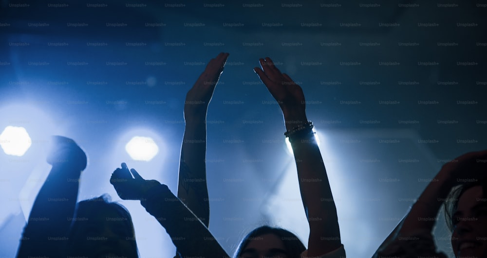 両手を上げてください。美しい照明のナイトクラブでダンスを楽しむ人々のグループ。