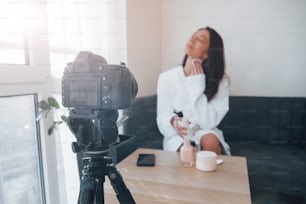 Backstage of the photoshoot. In front of camera on the tripod. Conception of fashion and skincare. Brunette girl uses cosmetics.