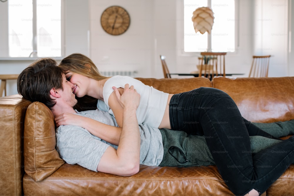 Passionate young couple cuddling smiling and looking at each other on comfortable couch at home