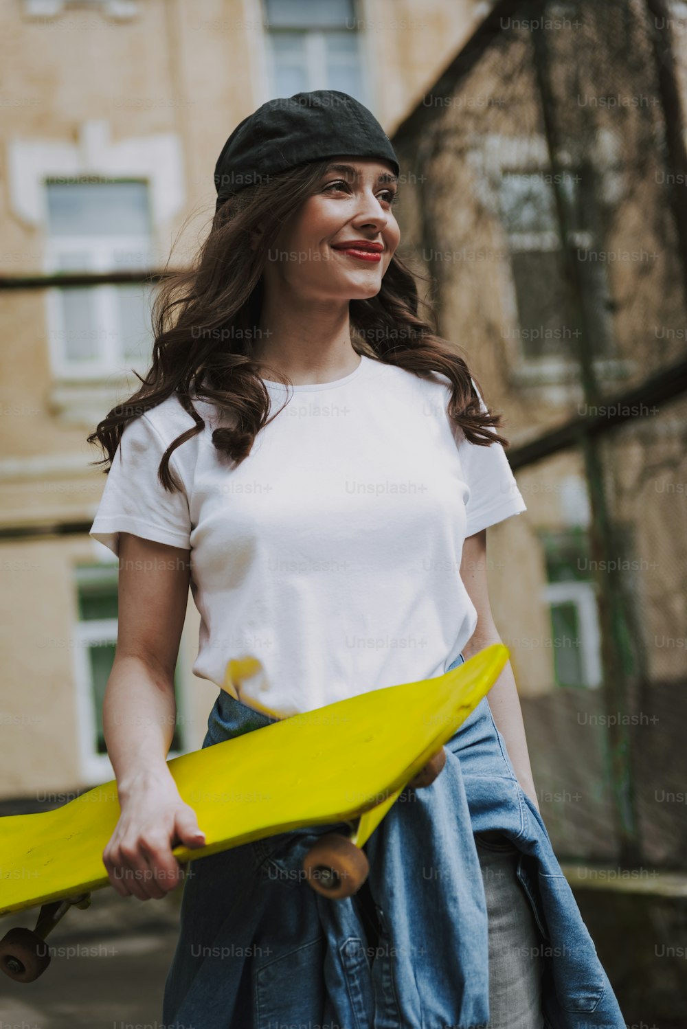 도시 생활 및 스포츠 활동. 노란 스케이트보드를 들고 도시 배경을 걷고 있는 젊은 세련된 힙스터 행복한 아가씨의 허리 초상화