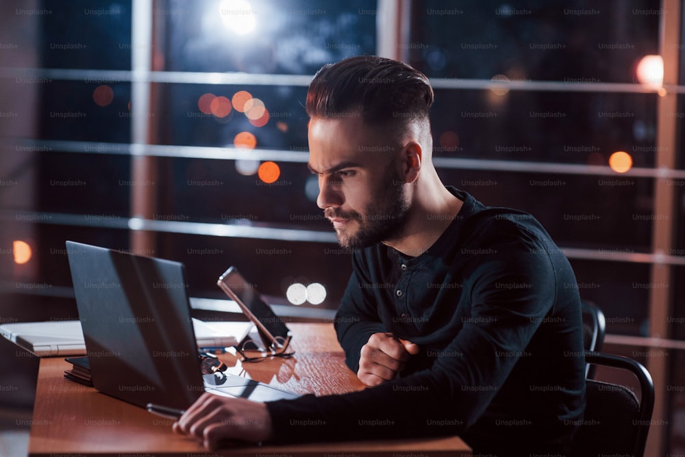 In the black wear. Stylish young businessman works alone in the office at nightime.