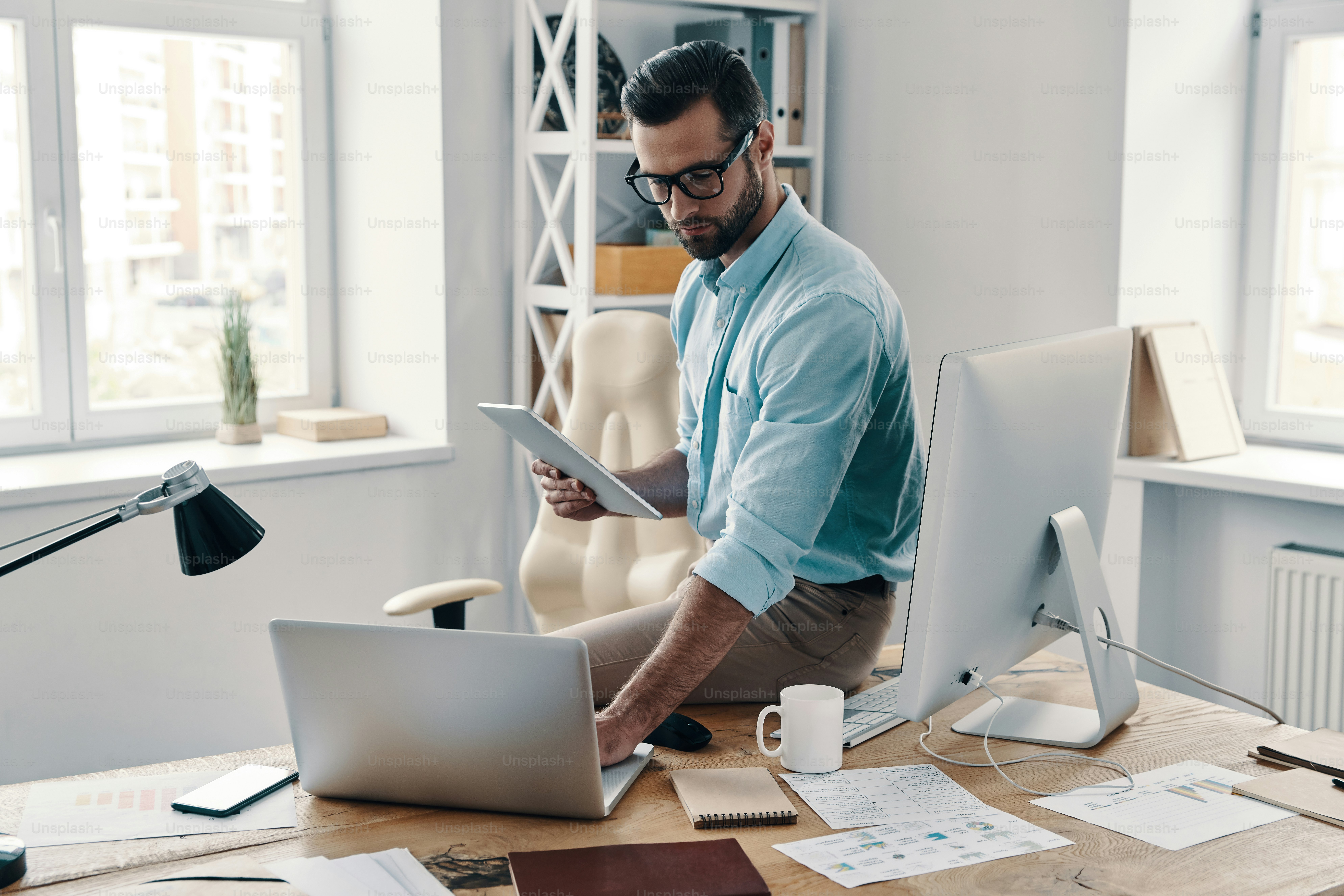 Young modern businessman using digital tablet and laptop while working in the office