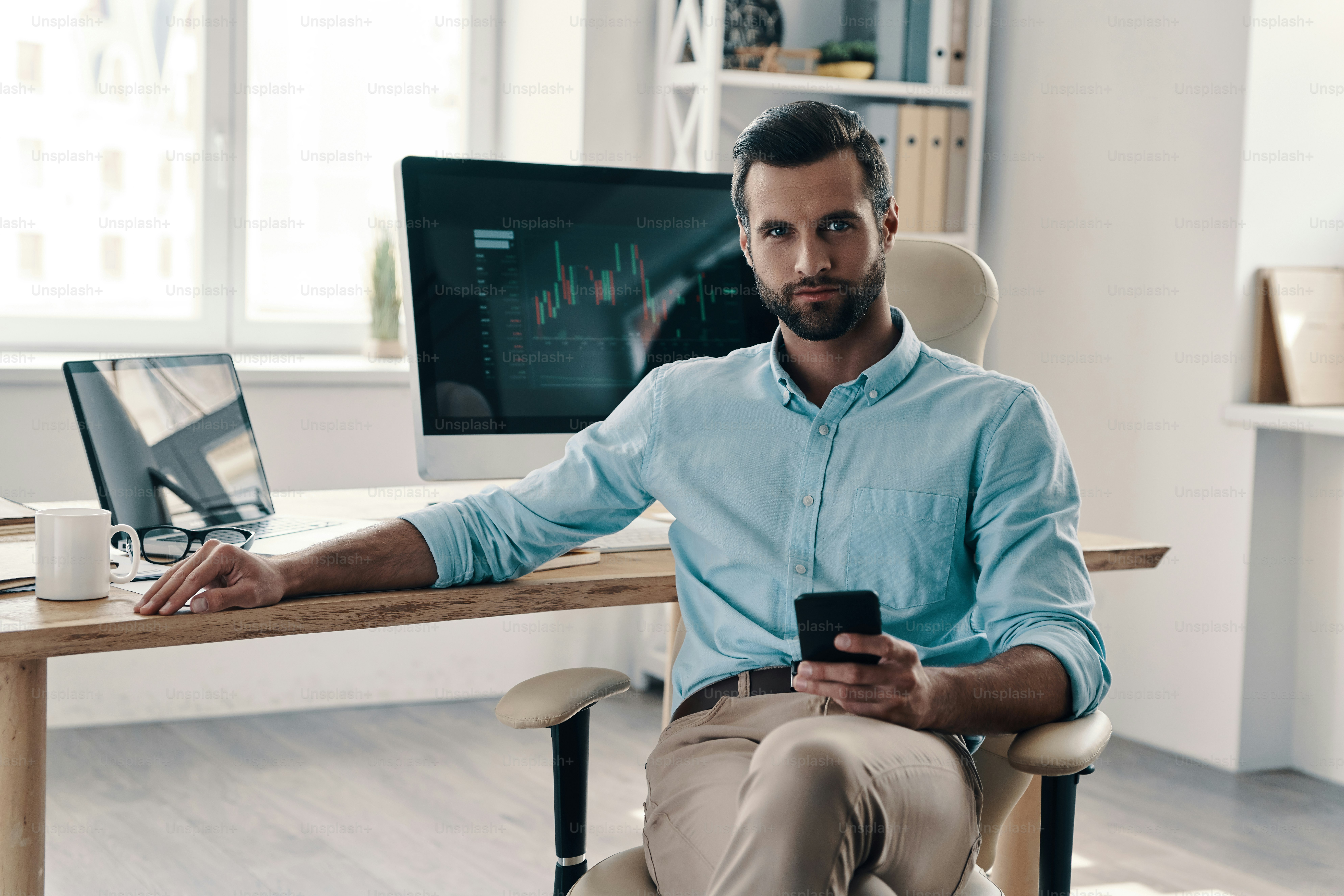 Young modern businessman looking at camera while sitting in the office