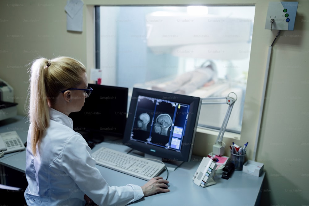 Radiologist analyzing brain MRI scan results of a patient on computer monitor in control room.