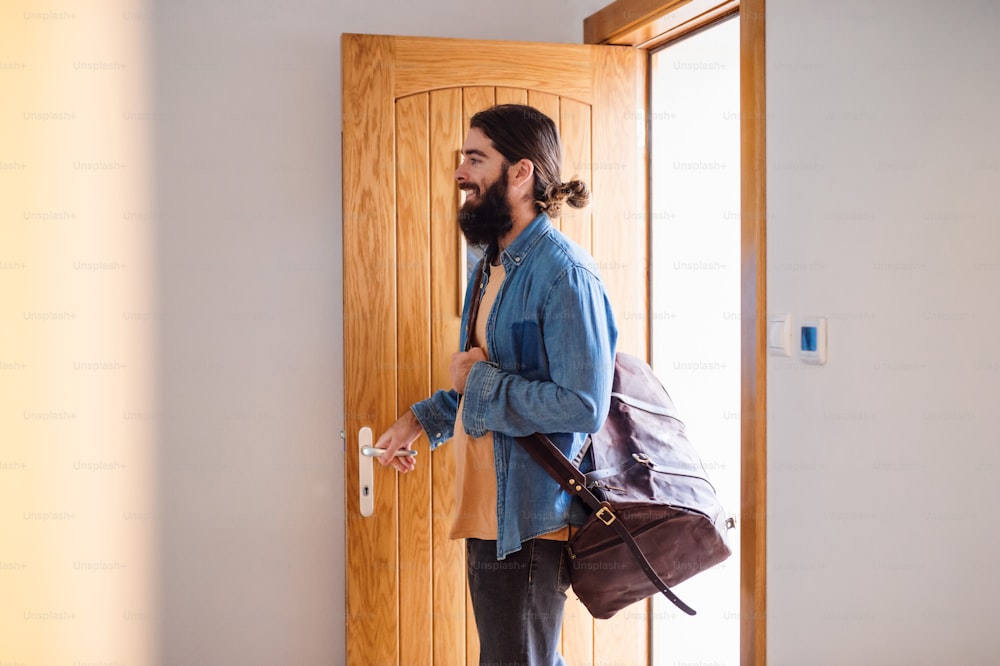 A young hipster man with bag entering front door when coming back home.