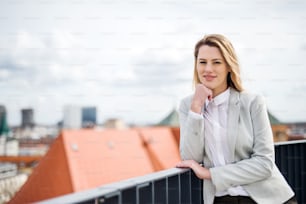 A portrait of young blond businesswoman standing outdoors on terrace outside office. Copy space.