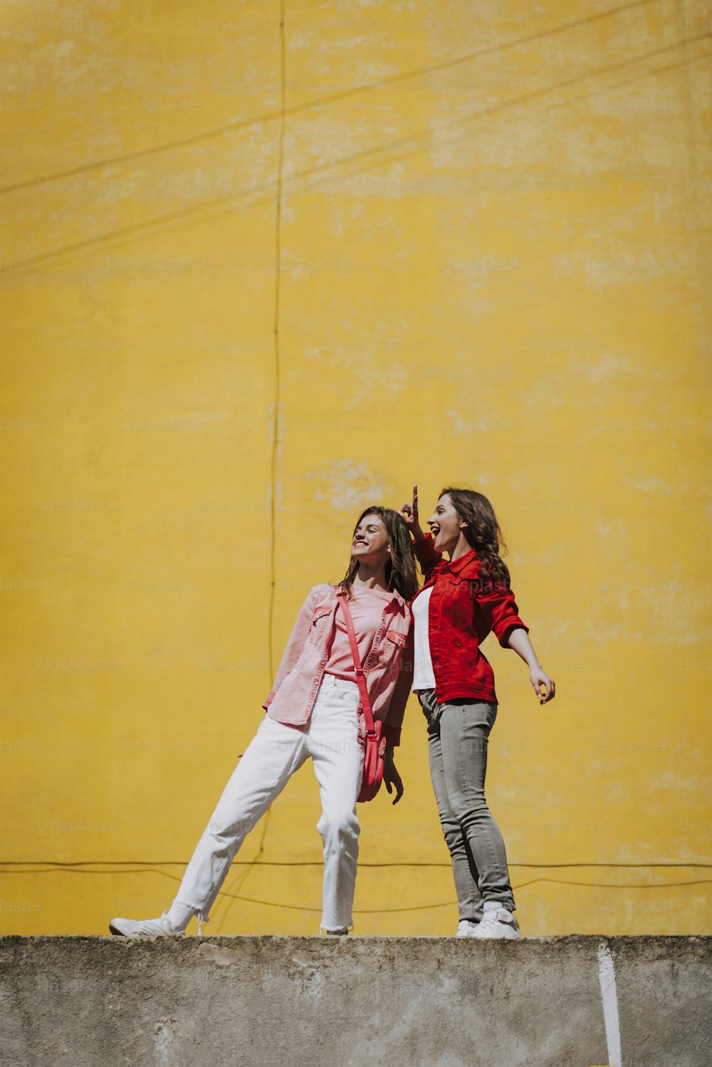 Urban lifestyle concept. Full length portrait of two happy young hipster ladies having fun together while staying on parapet
