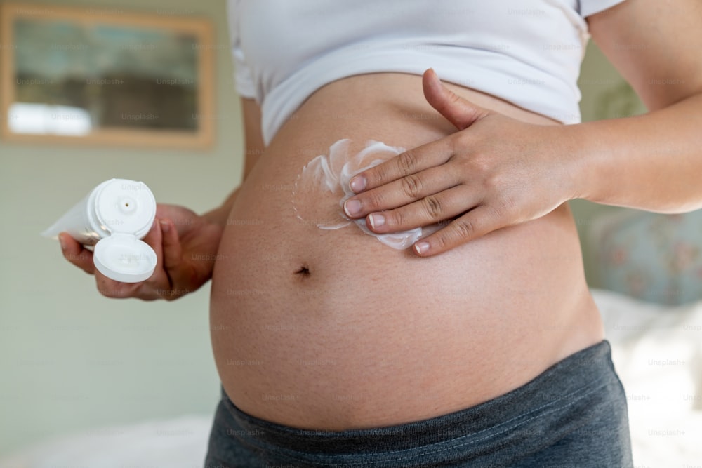 幸せな妊婦は、妊娠線を防ぐために妊娠中のお腹にスキンケアクリームローションを塗ります。健康的なスキンマッサージトリートメントとモイスチャーケアのコンセプト。
