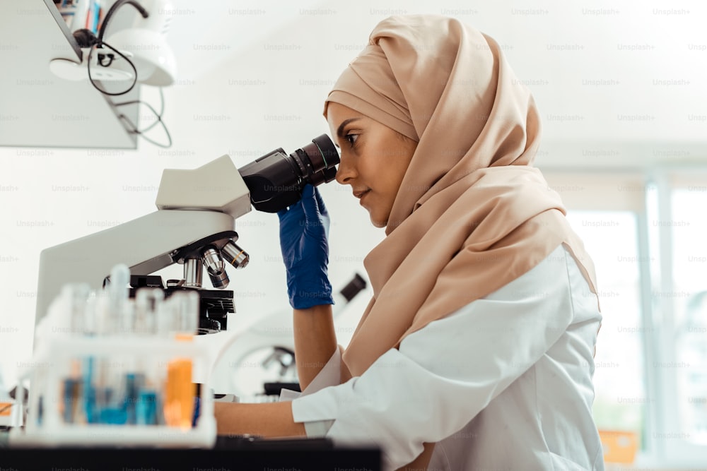 献身的な科学者。顕微鏡の前に座って研究に集中する知的な若い女性