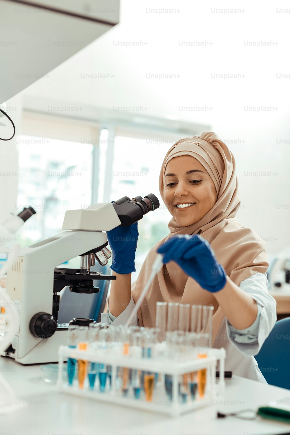 Profesión importante. Mujer musulmana positiva sonriendo mientras disfruta de su trabajo en el laboratorio