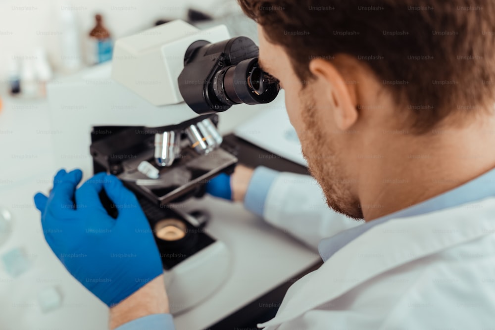 Investigación biológica. Vista superior de un hombre inteligente mirando al microscopio mientras realiza una investigación biológica