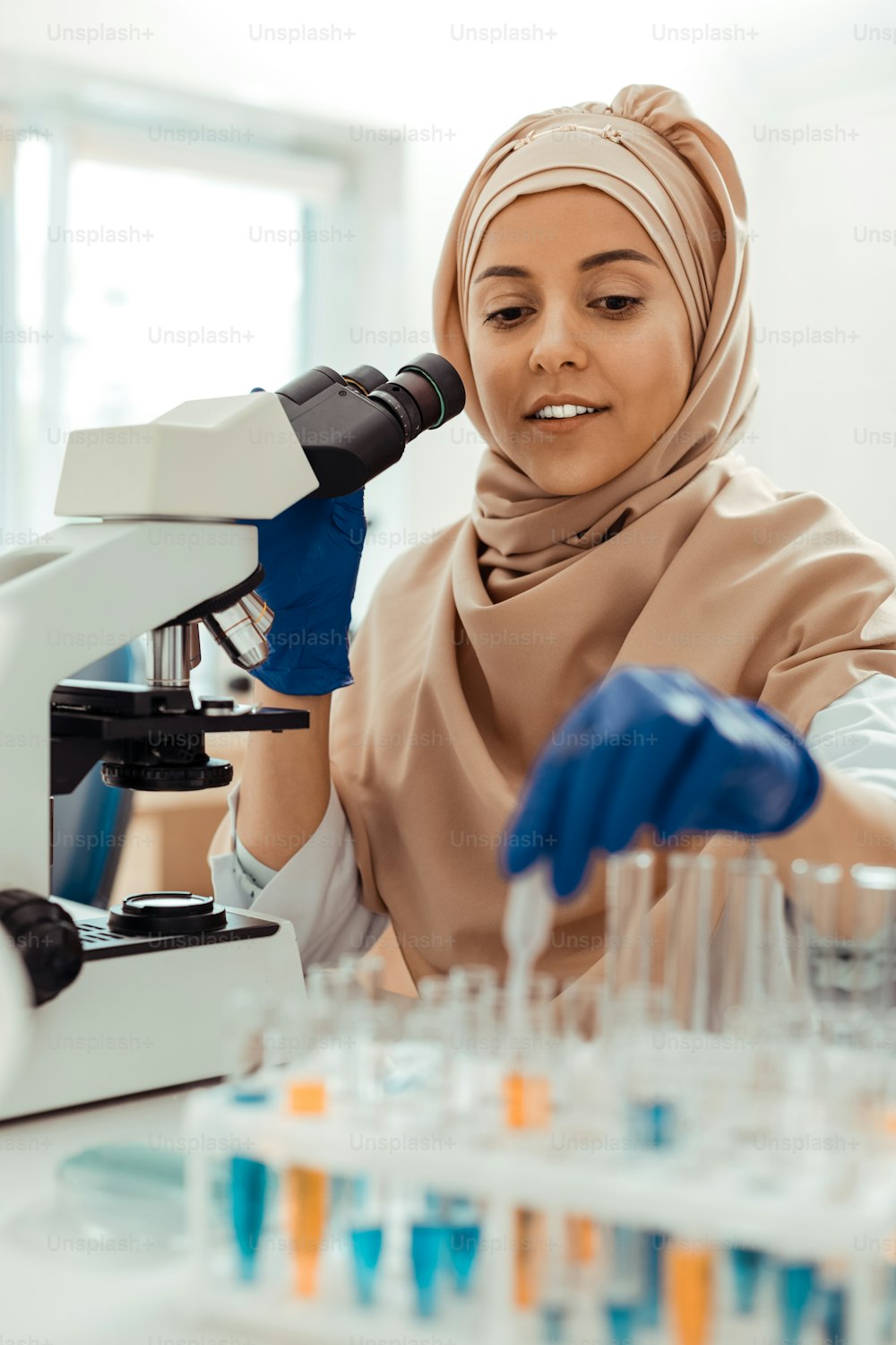 Professional research. Positive muslim woman sitting in front of the microscope while studying test samples in the lab