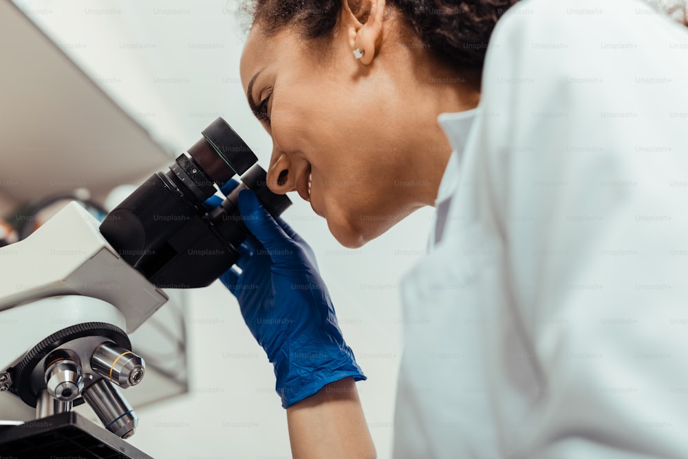 특수 장비. 생물학 실험실에서 일하면서 현미경을 사용하는 전문 여성 과학자의 낮은 각도
