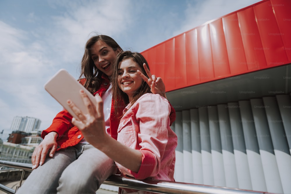 Urban lifestyle concept. Close up portrait of young happy hipster female friends having fun while making selfie on mobile phone on city ramp rails