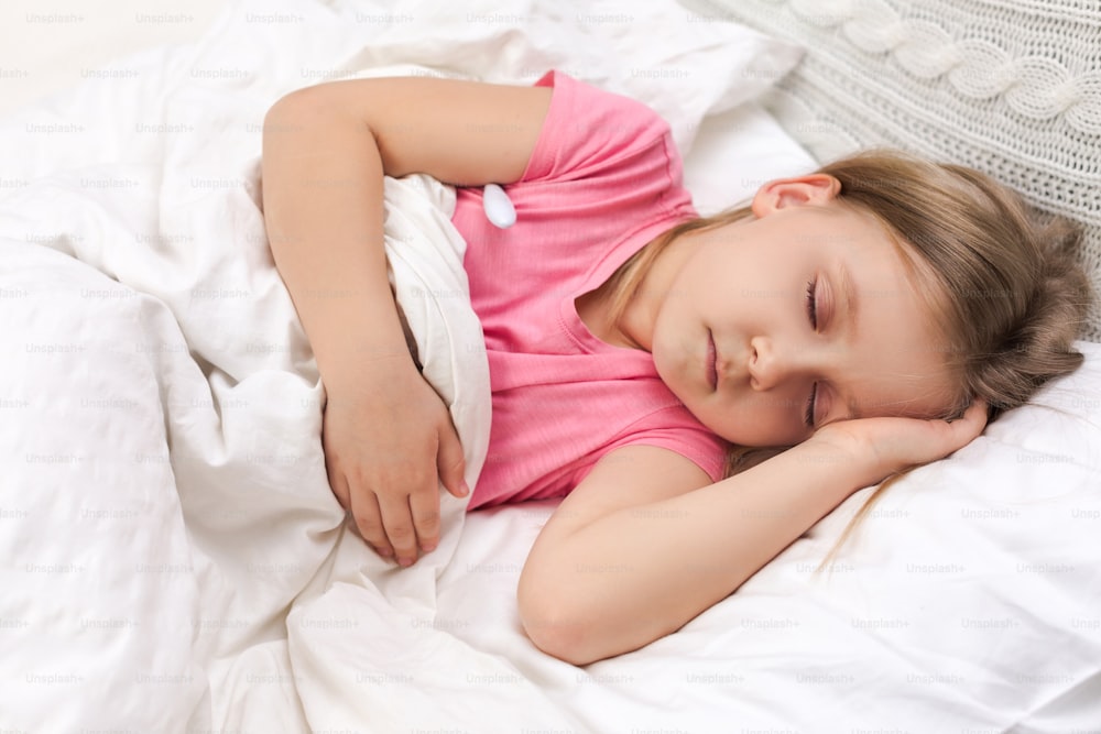 体温計を持ってベッドに横たわっている病気の小さな子供の女の子。風邪インフルエンザの季節