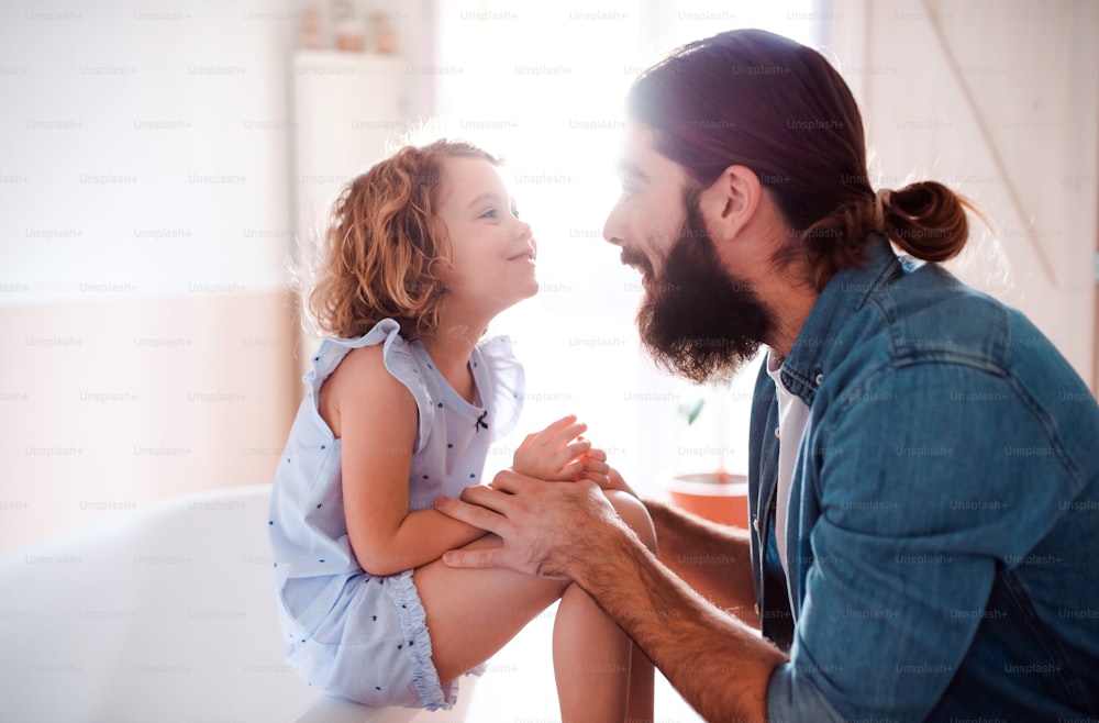 Una linda niña pequeña con un padre joven en casa, hablando.