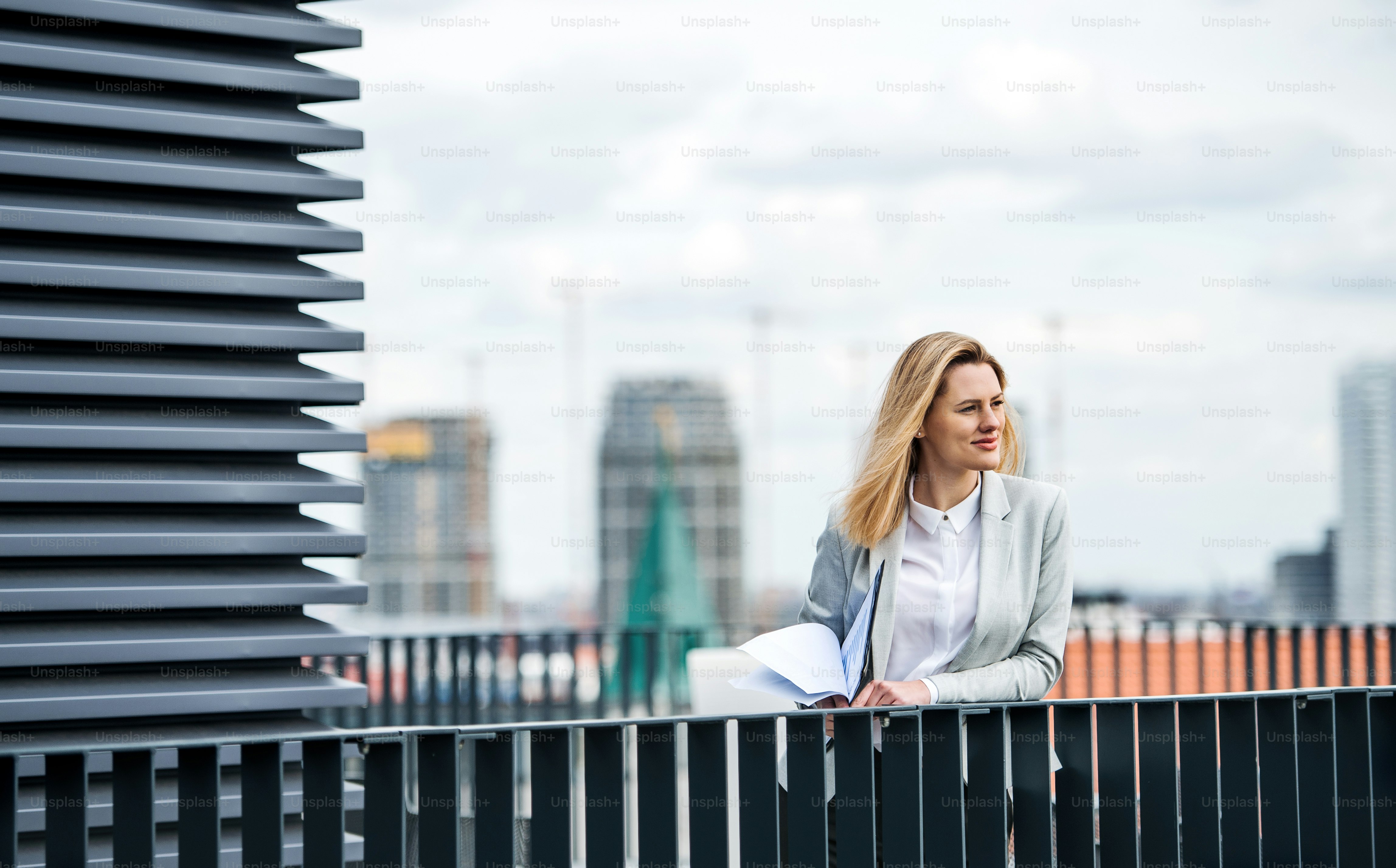 A portrait of young blond businesswoman standing outdoors on terrace outside office. Copy space.