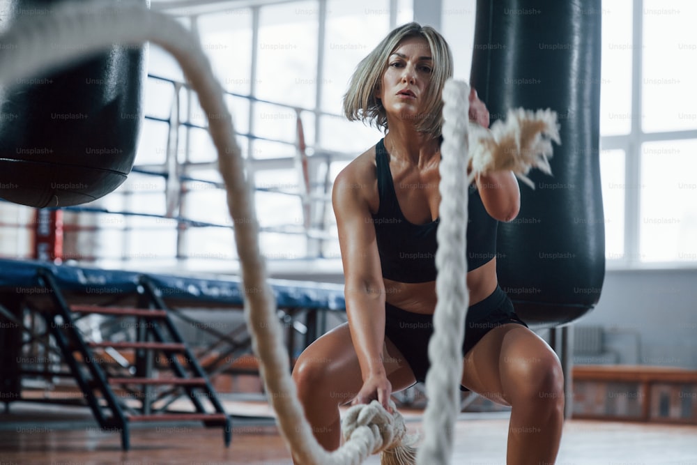 At the morning time. Blonde sport woman have exercise with ropes in the gym. Strong female.
