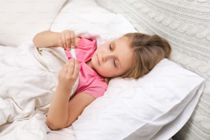아픈 어린 소녀가 온도계로 침대에 누워 있습니다. 감기 독감 시즌