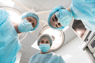 Bottom view of three professional doctors in medical clothes leaning to their patient and frowning
