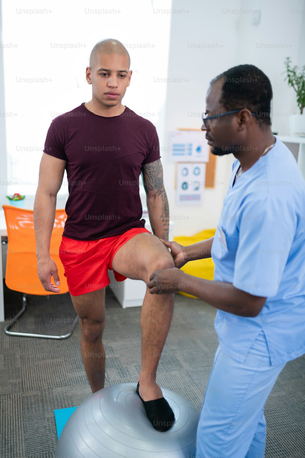 膝の検査。セラピストは、重傷を負った後、フィットボールの近くに立っているボディービルダーの膝を検査します