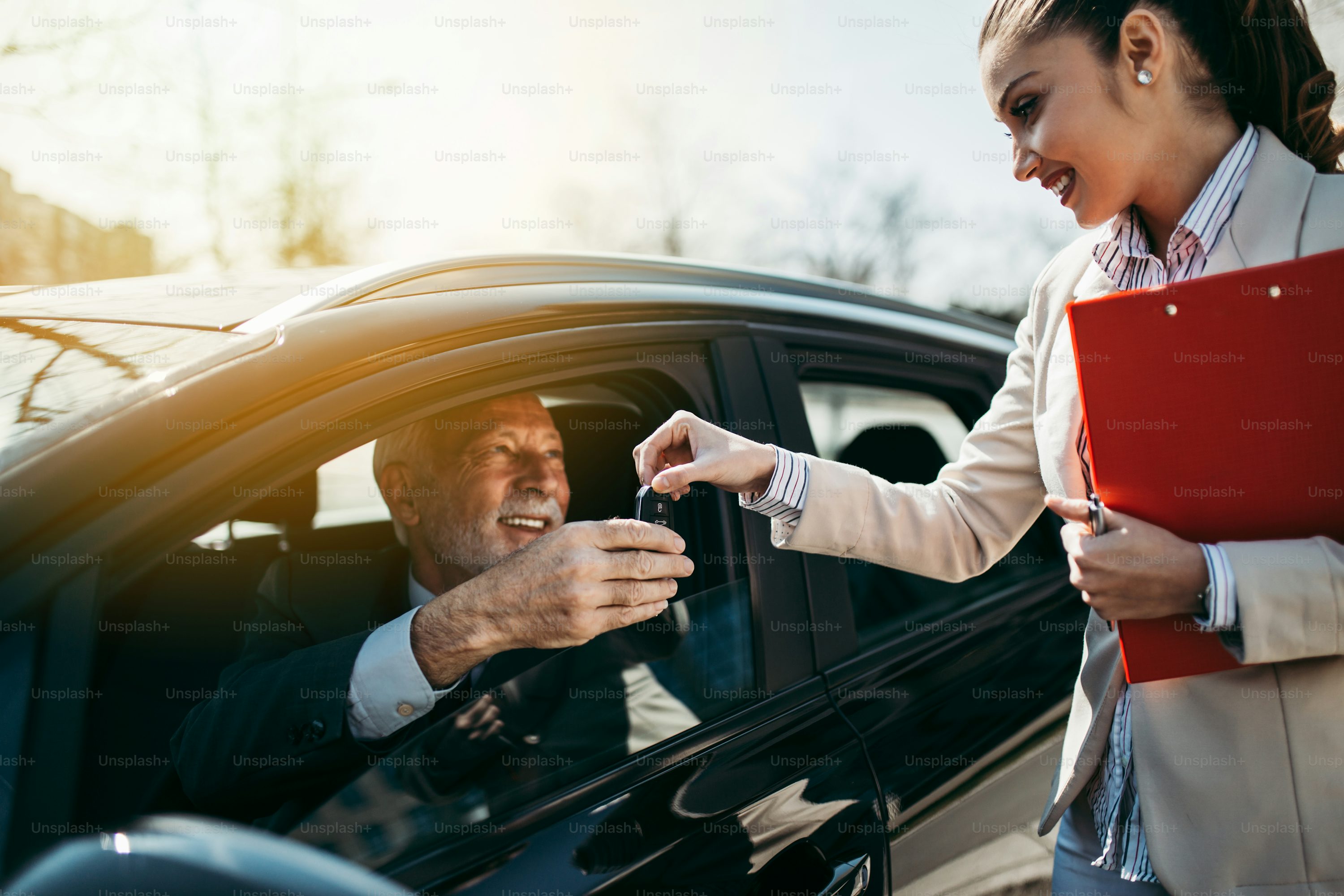 Beautiful young woman sales manager showing car specification to happy senior man buyer.