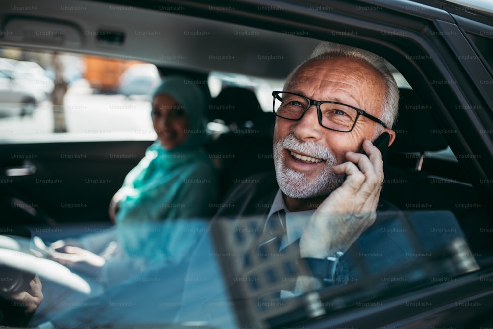 Beautiful muslim arabian woman with hijab sitting on backseat in luxury car together with senior business man. She using her laptop.