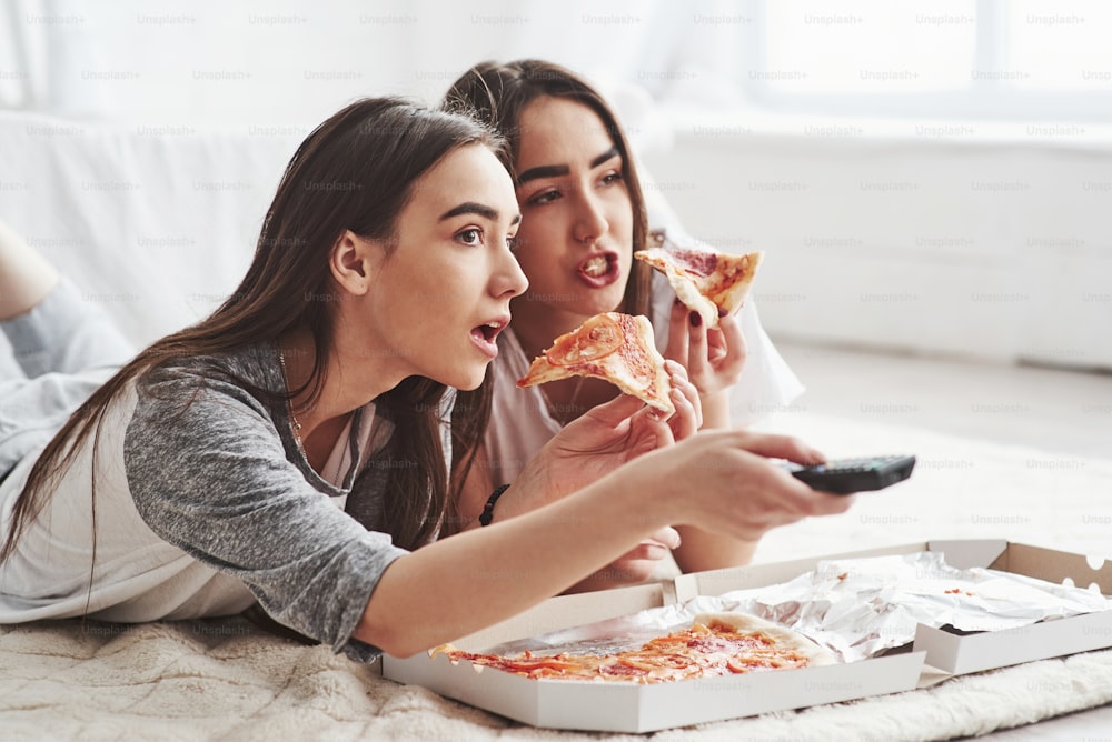No way, did you saw that. Sisters eating pizza when watching TV while lying on the floor of beautiful bedroom at daytime.