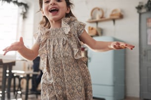 Happy smiling child runs at the kitchen at weekend time. Parents stands behind.