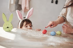Table is in the flour. Mother and daughter in bunny ears at easter time have some fun in the kitchen at daytime.