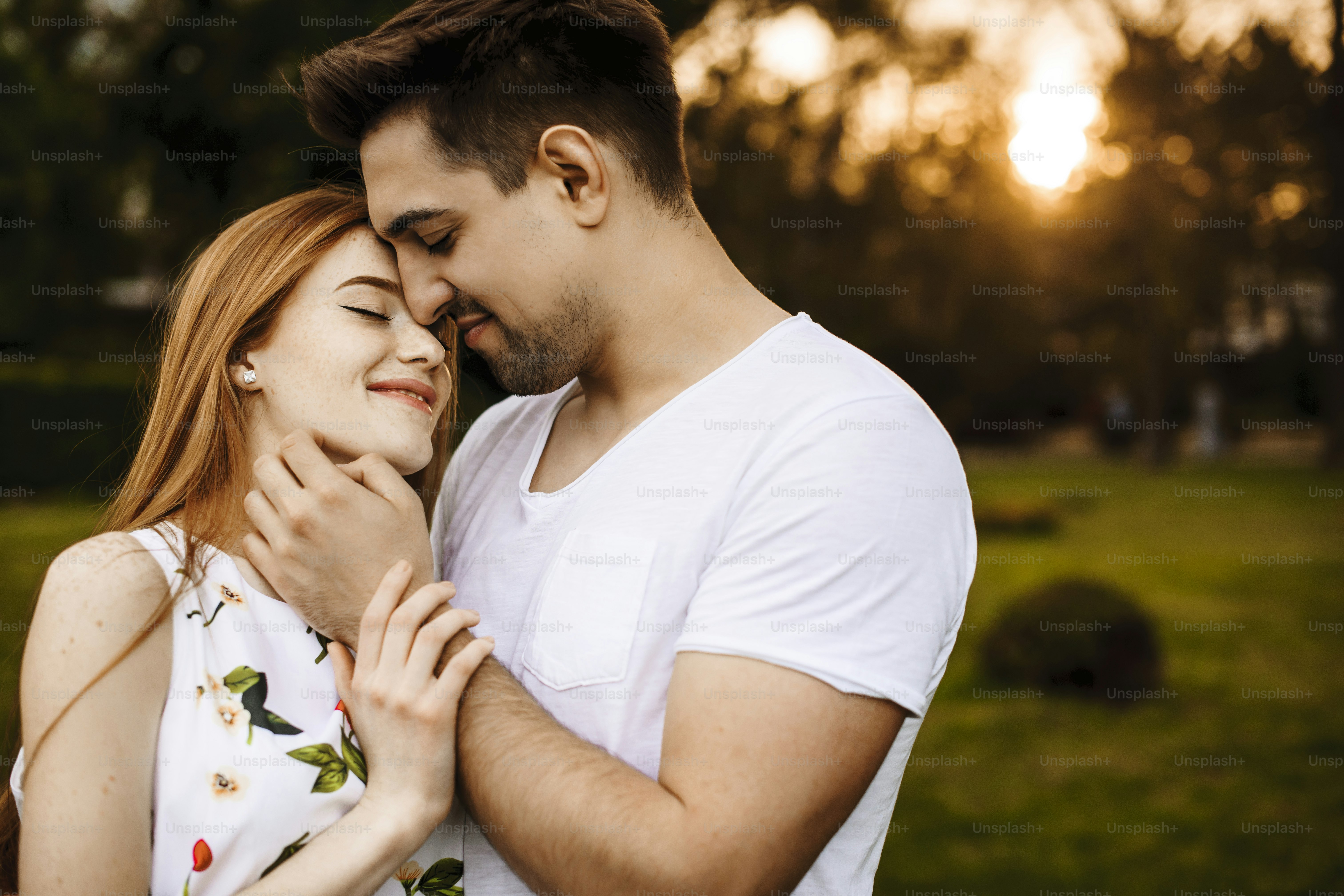 Handsome young man embracing her girlfriend smiling and touching her face while dating against sunset outside in their vacation time.