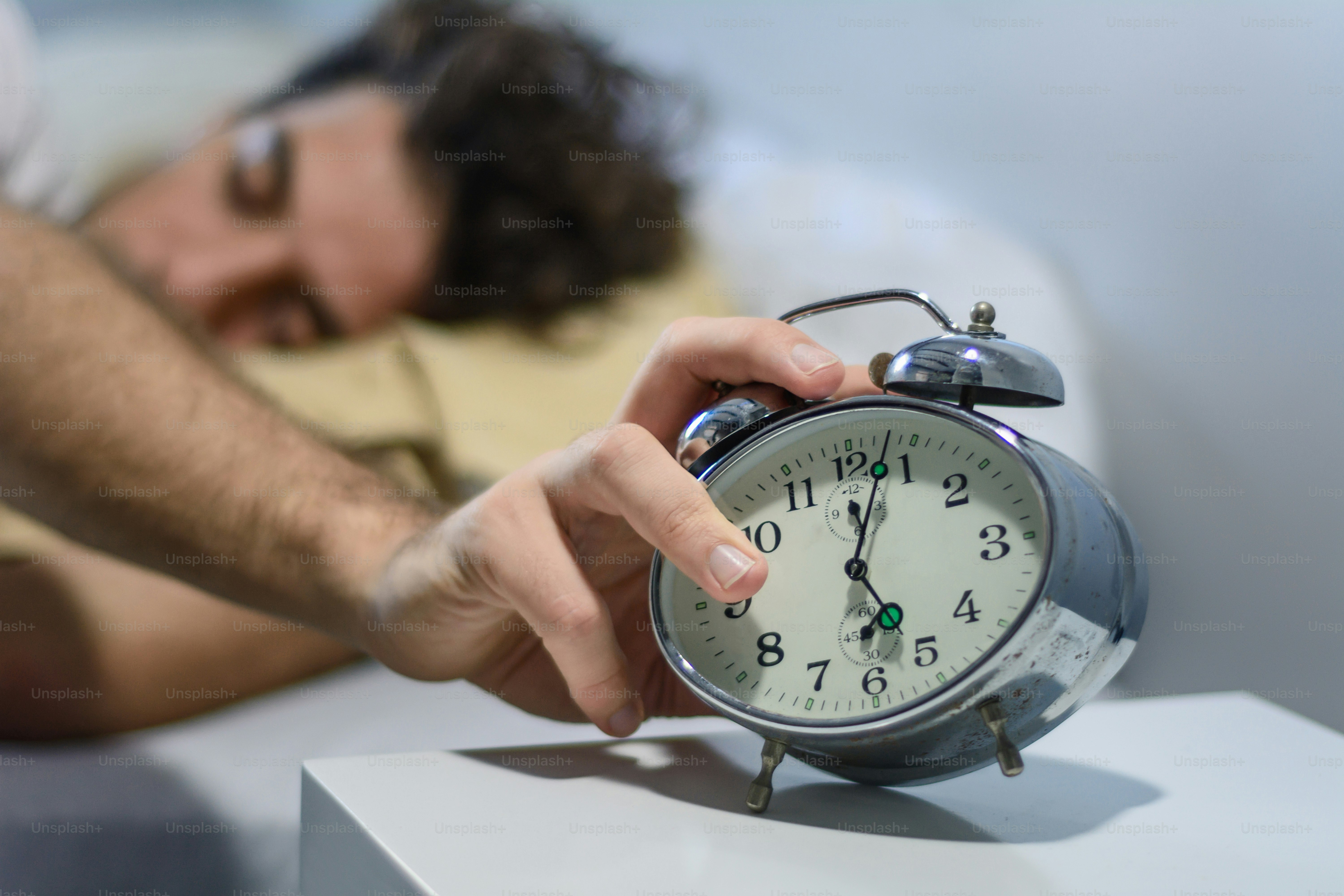 Frustrated young man woken-up by his alarm clock. Indoors