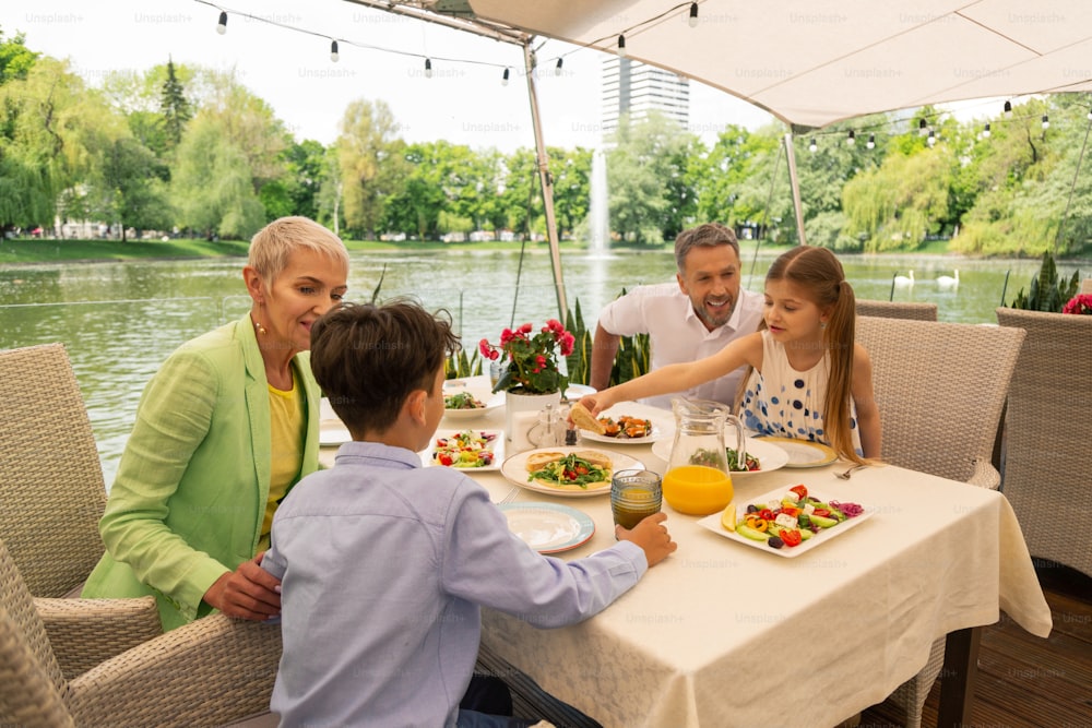 Petit-déjeuner avec les grands-parents. Garçon et fille se sentant excités en prenant le petit déjeuner avec les grands-parents près du lac