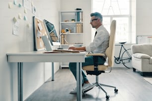 Thoughtful young man in shirt and tie working using computer while sitting in the office