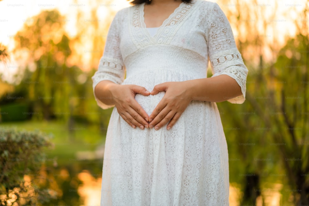 Schwangere Frau, die sich mit dem neuen Leben im Gartenhaus glücklich fühlt, während sie sich um ihr Kind kümmert. Die junge werdende Mutter hält Baby im schwangeren Bauch. Schwangerschaftsvorsorge und Schwangerschaftskonzept für Frauen.