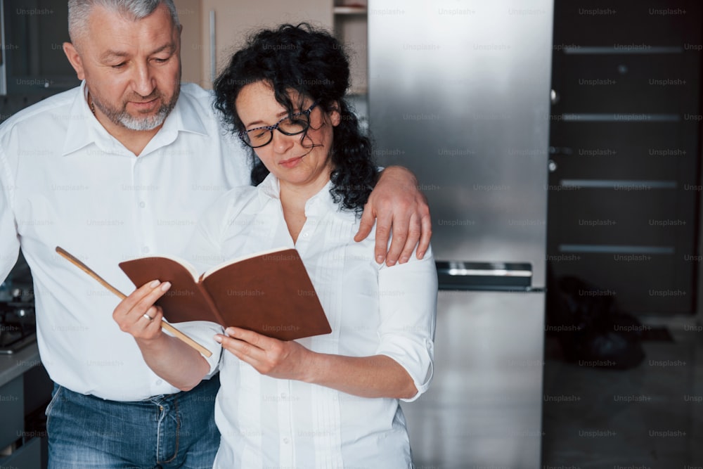 Attention needed. Man and his wife in white shirt preparing food on the kitchen using vegetables.