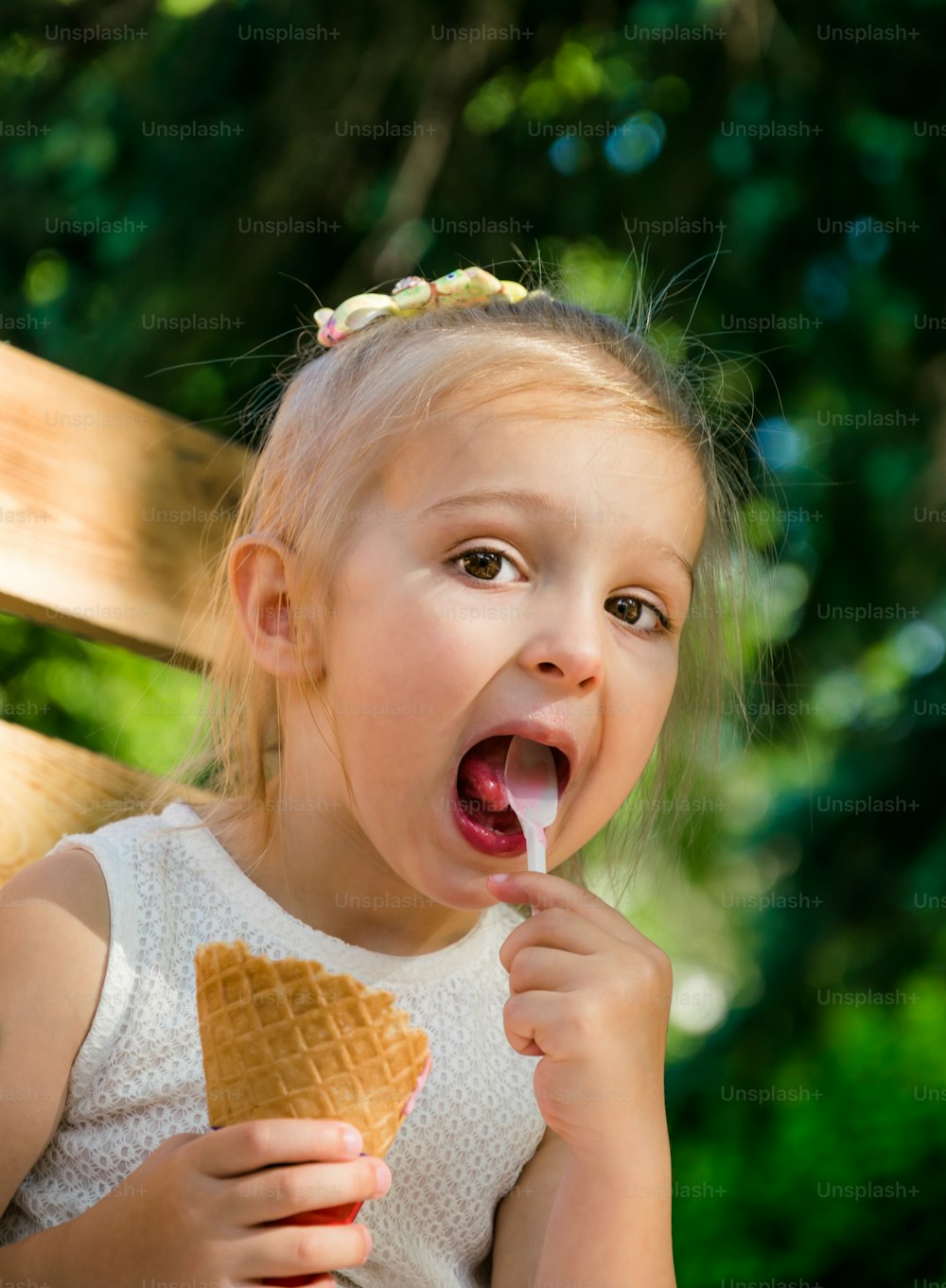little funny girl of three years old laughs and eats strawberry ice cream in a cone. Children's summer holiday in the park