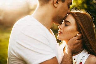 Retrato de perto incrível de uma linda garota de cabelo vermelho com sardas com olhos fechados beijados por seu namorado na testa contra o pôr do sol durante a viagem.