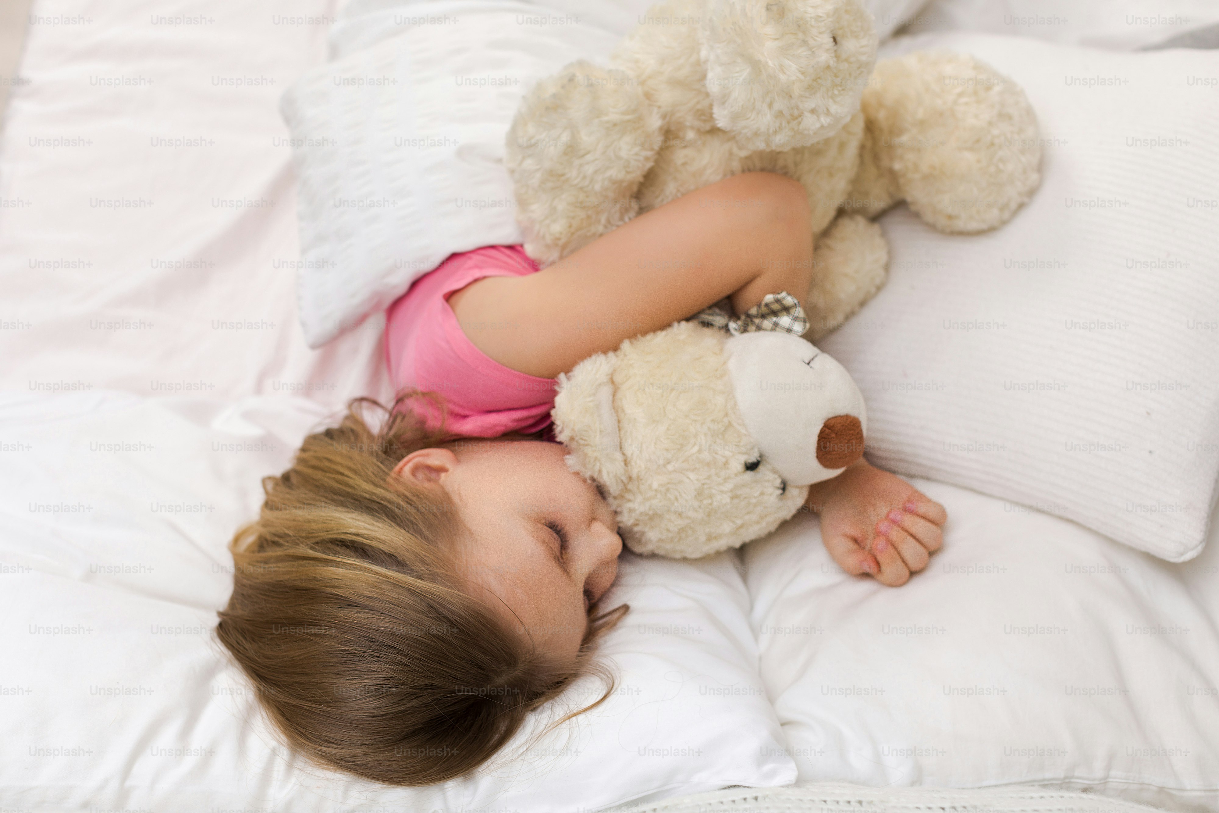 Cute little child girl sleeping with teddy bear in her bed