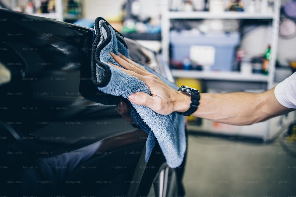 Un uomo che pulisce l'auto con un panno in microfibra, concetto di dettaglio dell'auto (o valeting). Messa a fuoco selettiva.