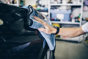 Un uomo che pulisce l'auto con un panno in microfibra, concetto di dettaglio dell'auto (o valeting). Messa a fuoco selettiva.