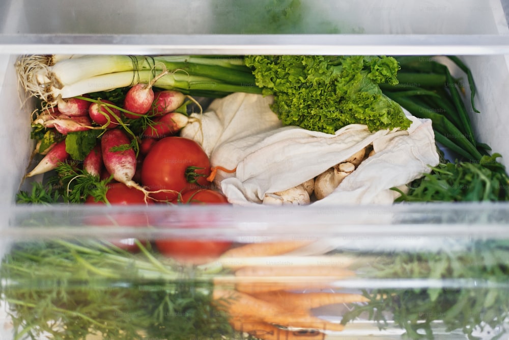 Spesa a spreco zero in frigorifero. Verdure fresche in cassetto aperto in frigorifero. Carote, pomodori, funghi, ravanelli, insalata, rucola, concetto di shopping a rifiuti zero. Dieta vegetariana