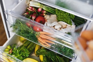 Spesa a spreco zero in frigorifero. Verdure fresche in cassetto aperto in frigorifero. Carote, pomodori, funghi, ravanelli, insalata, rucola, concetto di shopping a rifiuti zero. Dieta vegetariana