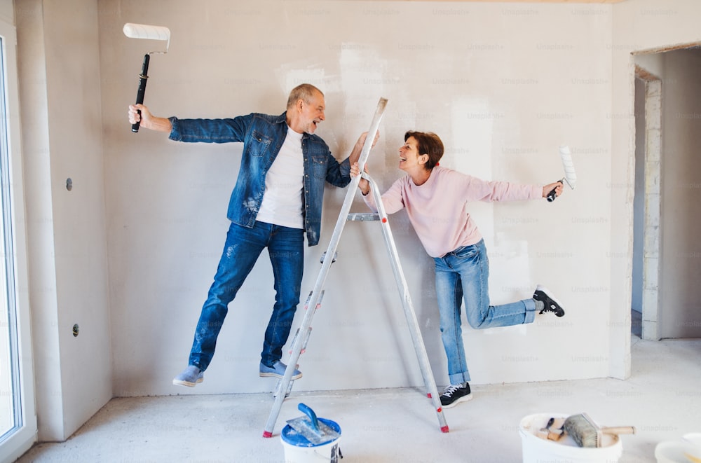 Retrato de una alegre pareja de ancianos pintando paredes en una nueva casa, divirtiéndose. Concepto de reubicación.