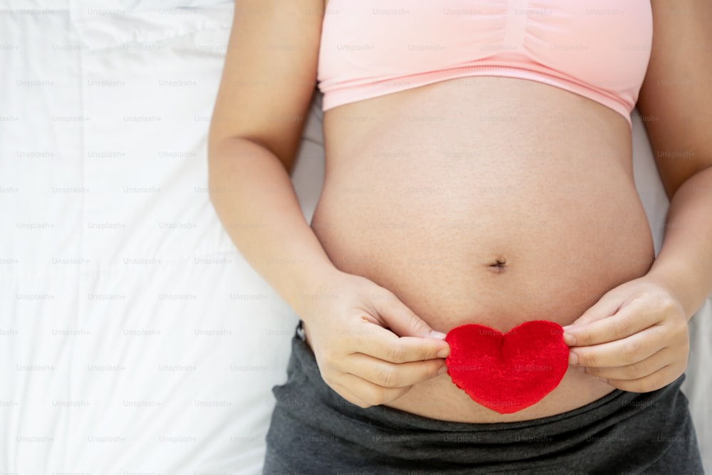 Pregnant woman feeling happy at home while taking care of her child. The young expecting mother holding baby in pregnant belly. Maternity prenatal care and woman pregnancy concept.