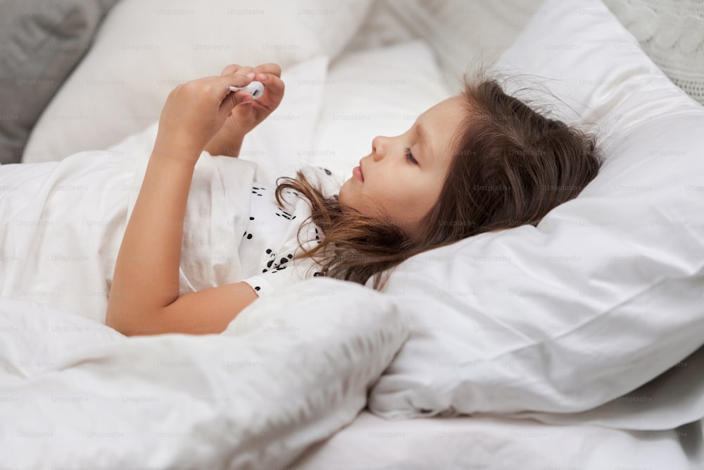 Sick little child girl lying in bed with thermometer. Cold flu season