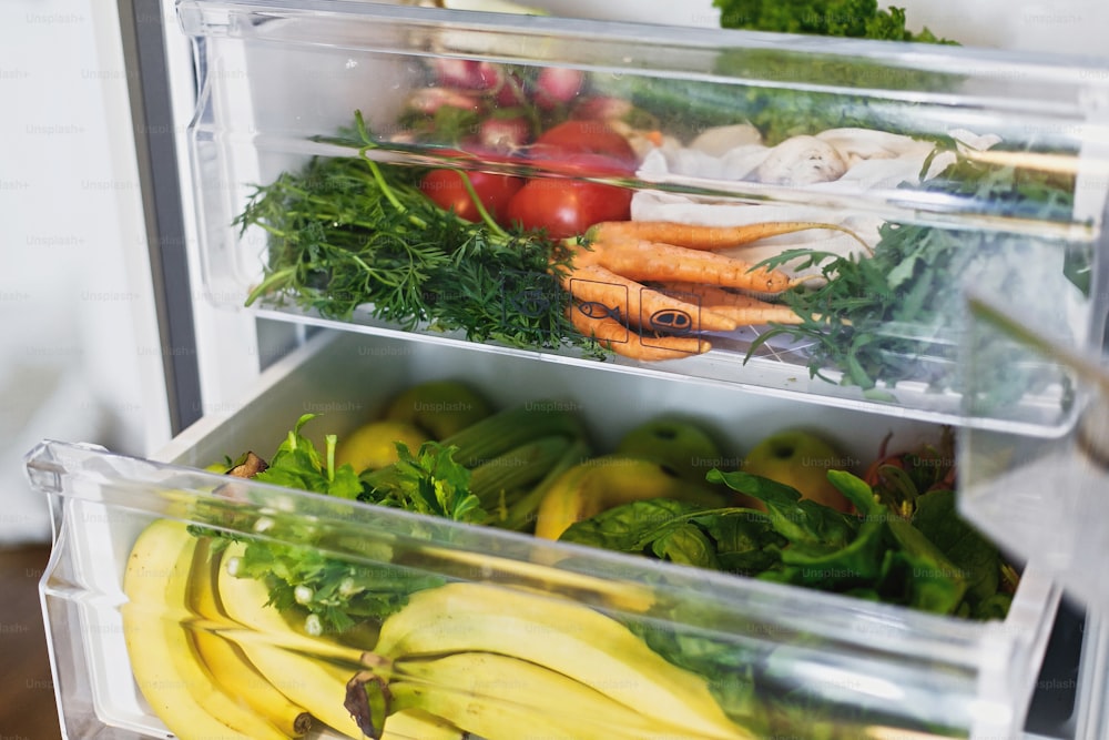 Zanahorias, tomates, champiñones, plátanos, ensalada, espinacas, apio, manzanas sin plástico en el refrigerador. Compras de comestibles sin desperdicio. Verduras frescas en el cajón abierto del refrigerador. Dieta vegetariana